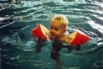 An old photo of a young child swimming with orange arm floats.