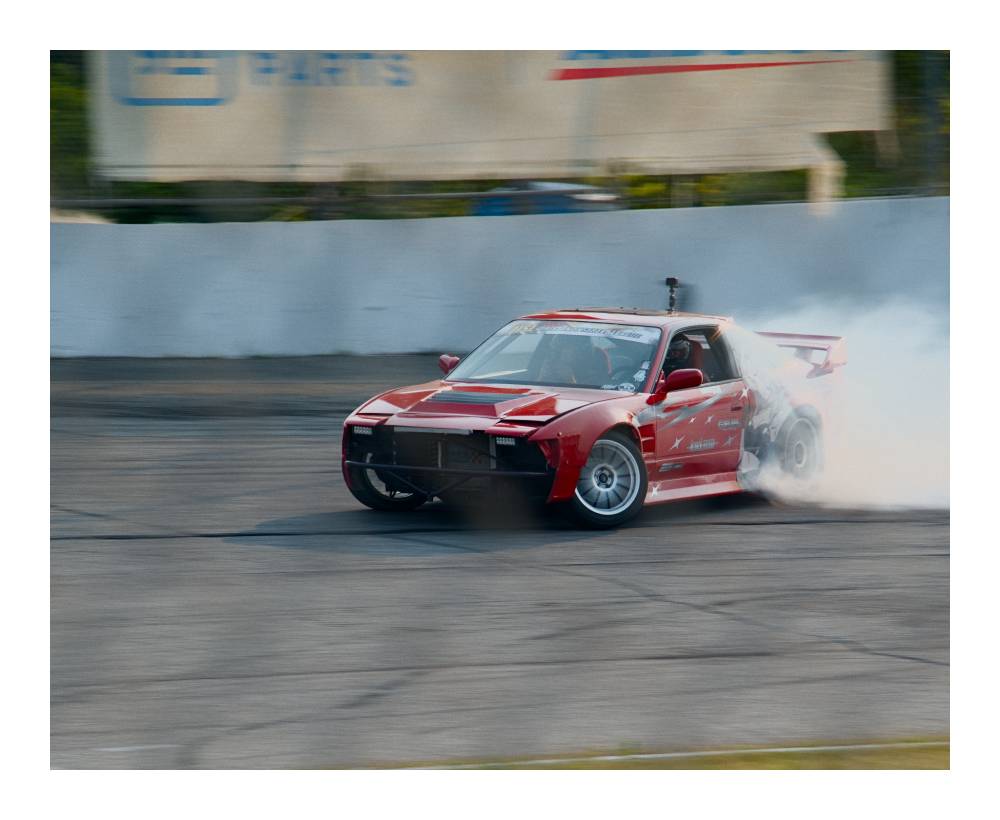 Red 80s Nissan with itasha drifting a corner, smoke pouring out of the back tires