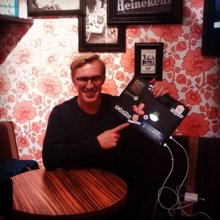 A man pointing at a laptop covered in stickers while sitting at a small table.
