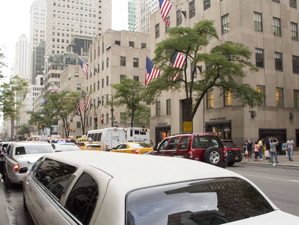 A white limousine and taxis fill a Fifth Avenue street lined with flags.