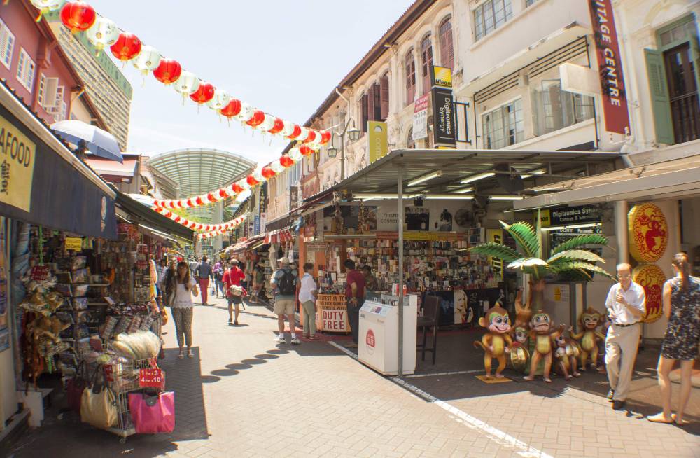 Shoppers browse market stalls beneath red lanterns strung across a Chinatown street.
