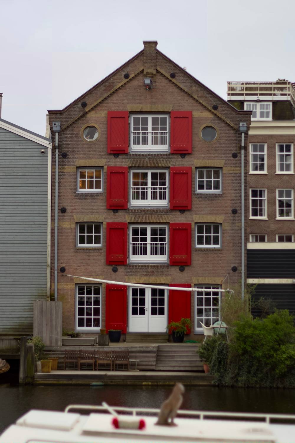 Four story building in the river front in Amsterdam with red wooden window slats