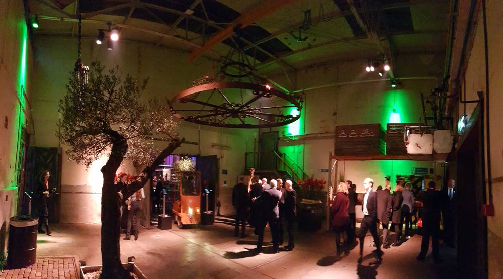 Guests mingle beneath string lights and an olive tree in an industrial hall at De Fabrique.