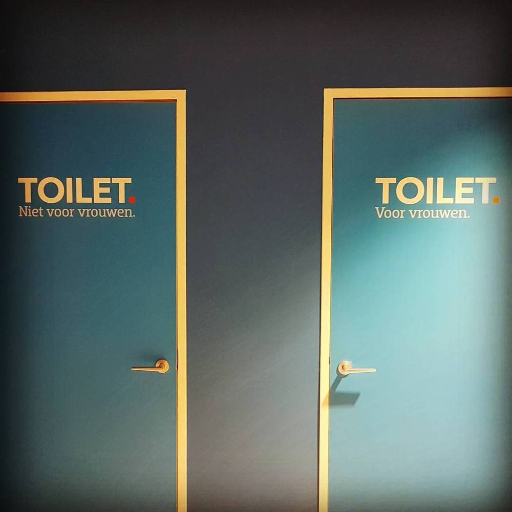 Two blue toilet doors, one labeled "Niet voor vrouwen" (not for women) and the other "Voor vrouwen" (for women).