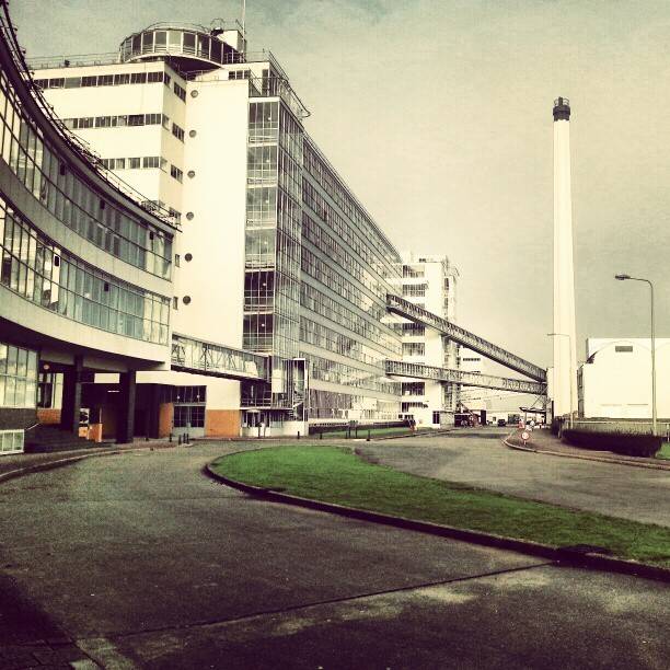 A curved modernist office building with a tall chimney, an example of Nieuwe Bouwen architecture.