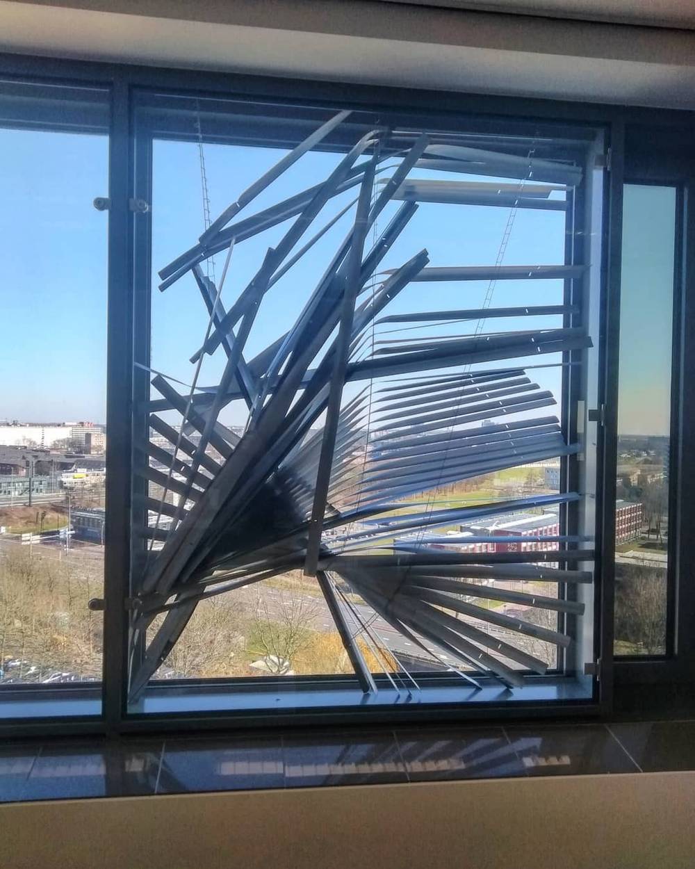 A window with angled reflective blinds, overlooking a modern building exterior.