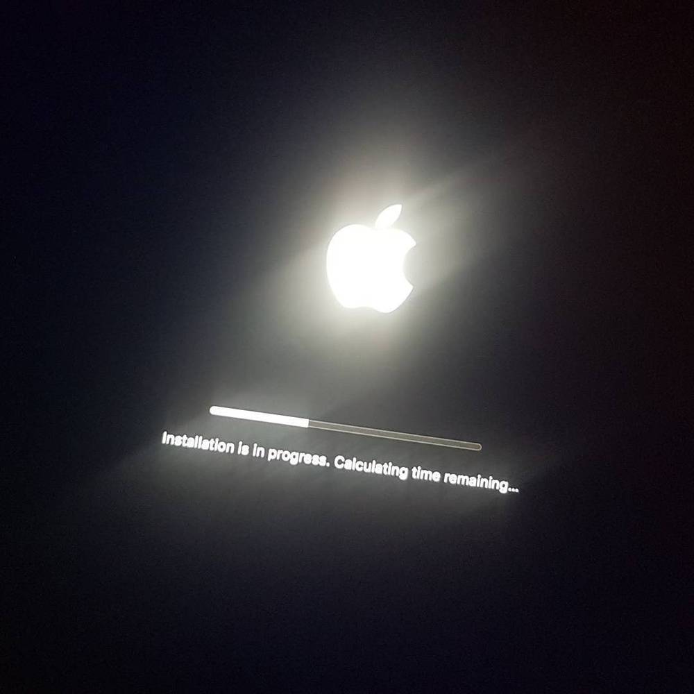 A laptop screen showing the Apple logo during a macOS software update, with a progress bar.