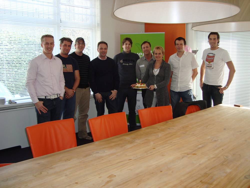 A group of colleagues posing around a conference table, one holding a cake with candles.