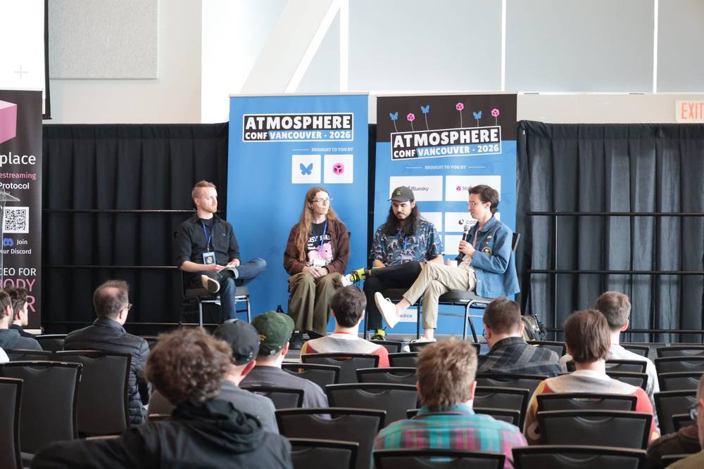 Four people take part in a panel discussion on a conference stage with AtmosphereConf Vancouver banners.