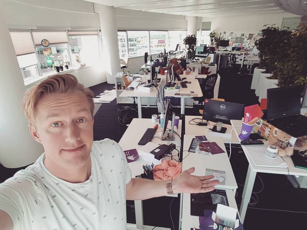 Selfie in an open-plan office, gesturing toward empty desks and computer screens on a Friday.