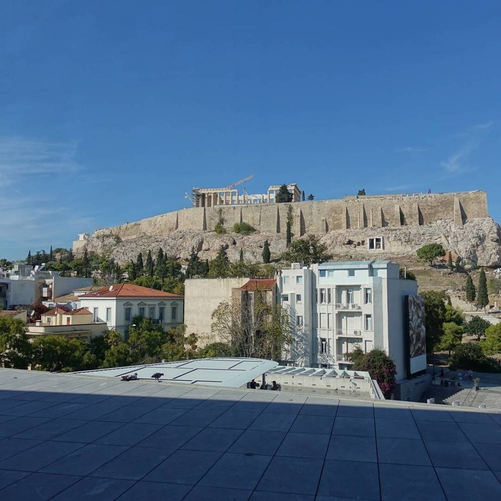 The Acropolis in Athens seen from a rooftop terrace, with the city spread out below.