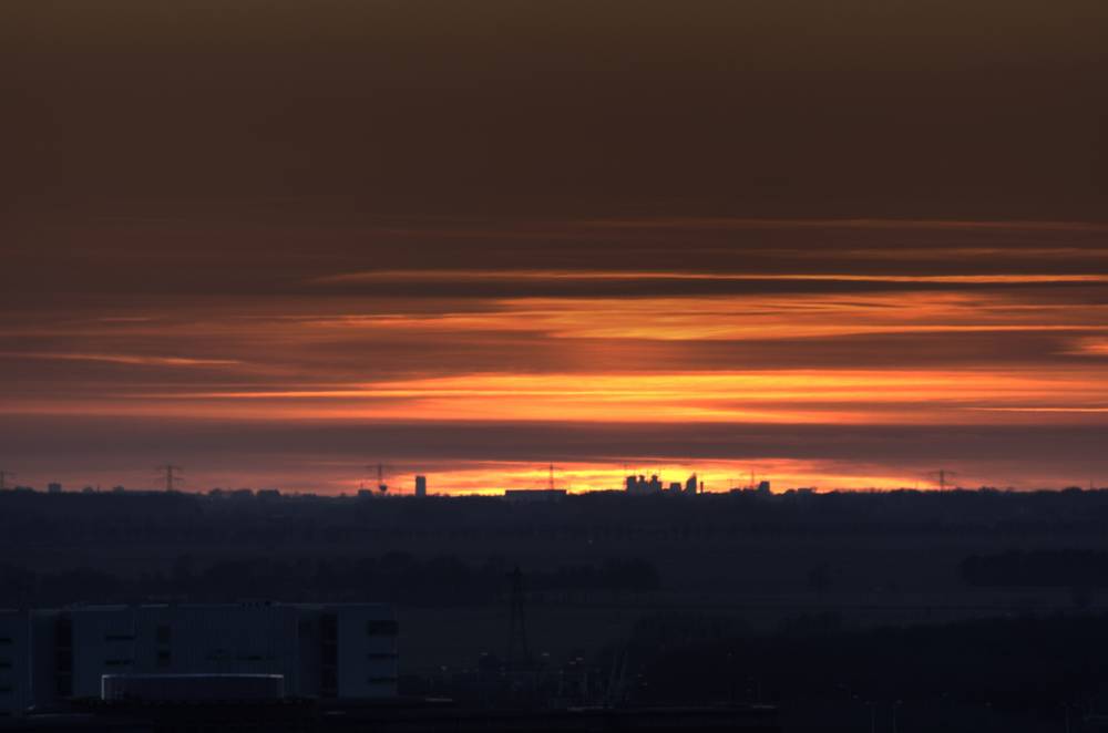 Streaks of orange sunset light stretch across a cloudy sky above rooftops.