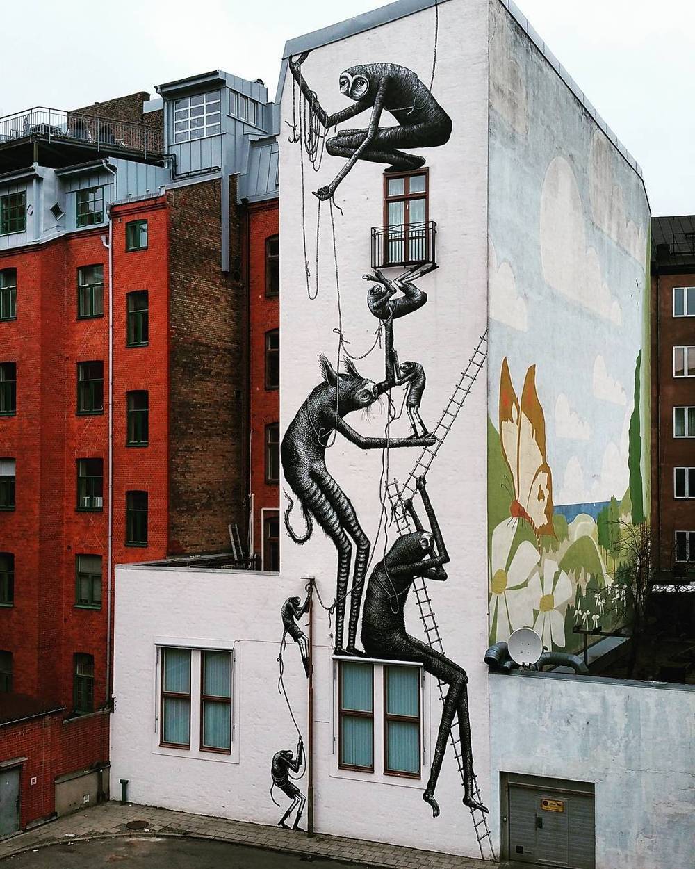 A building facade painted with a mural of stylized figures climbing ladders toward a flower.