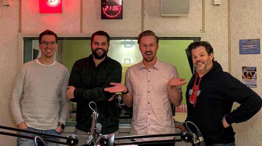 Four men pose together smiling in a radio studio.