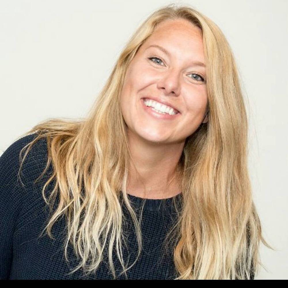A smiling blonde woman with long hair, in a dark top.
