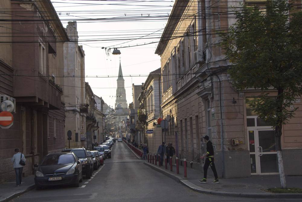 A quiet city street lined with historic buildings leading toward a distant church spire.