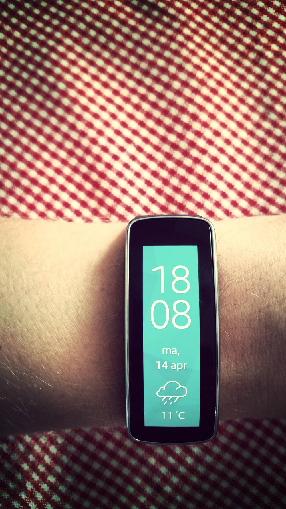 A Samsung Gear Fit smartwatch displays the time and weather on a wrist.