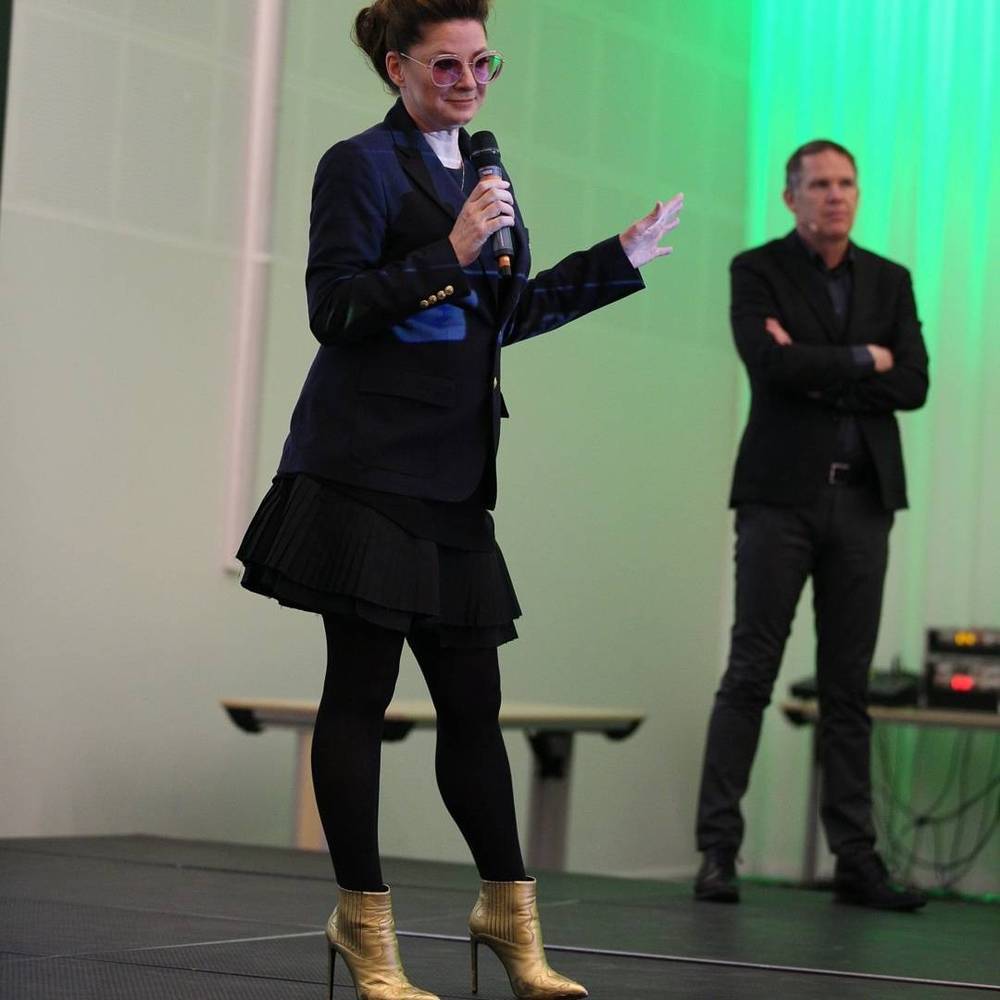 A woman and a man on stage together during a conference presentation with green lighting.