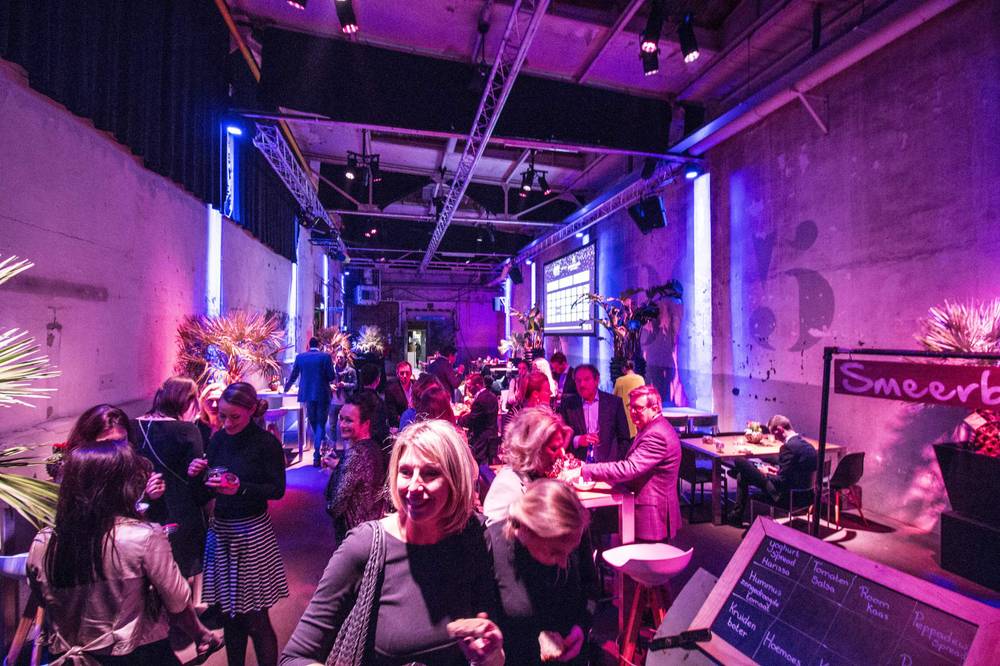 Guests mingle in a corridor lit in blue near a 'Smeerboel' sign at De Fabrique.