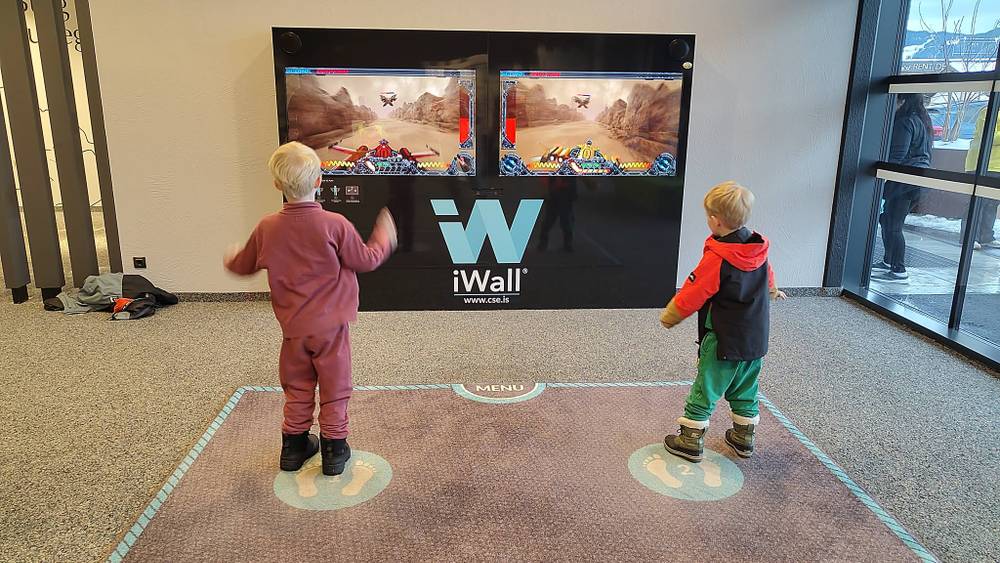 Two children play an interactive game on a large touchscreen wall.