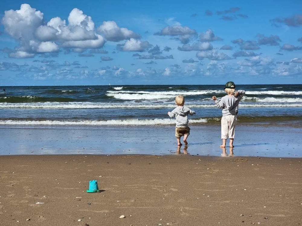 Two children playing in the ocean surf on a beach, with waves rolling in.