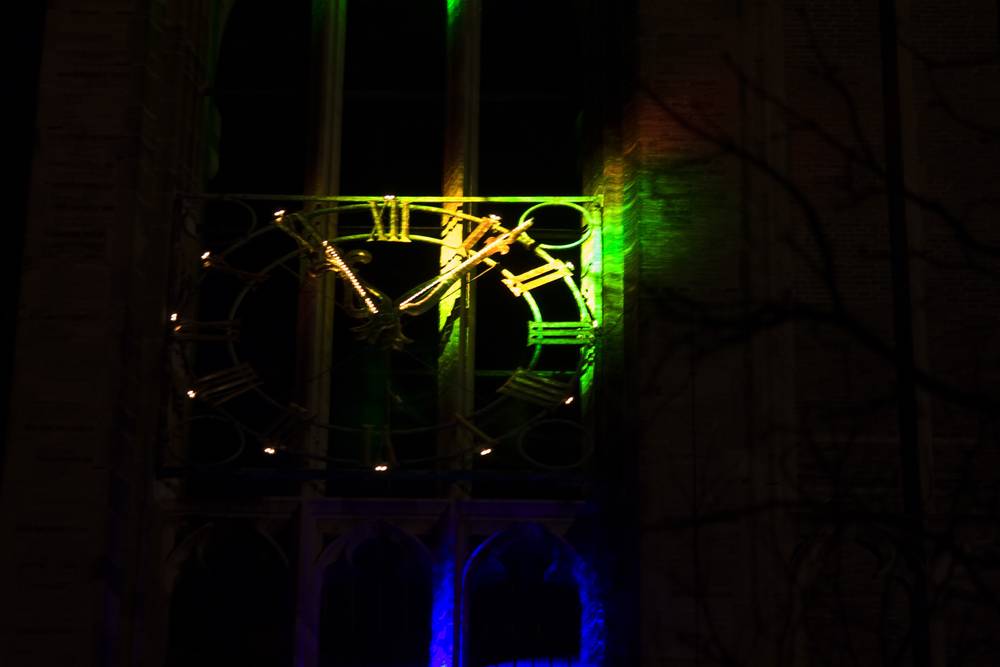A tower clock face is lit in green and gold during a light projection show.
