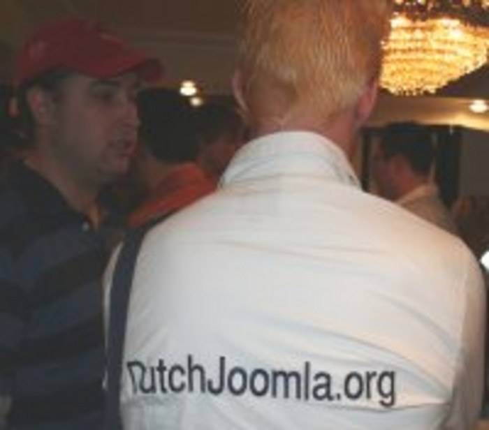 A man's back shows a jacket printed with 'DutchJoomla.org' at a reception.