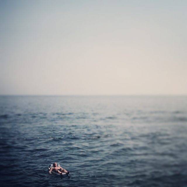 A calm expanse of sea with a person swimming in the distance.