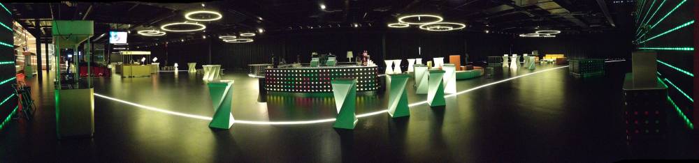 A dark event hall decorated with a glowing light path and green triangular sculptures.