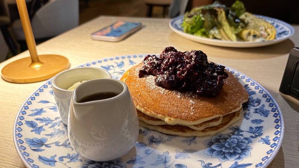 Pancakes with blueberry compote on an ornate blue and white plate, with syrup.