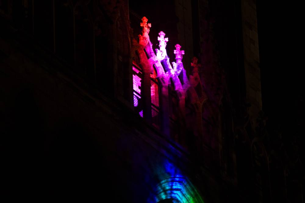 Pink and purple lights illuminate carved stone spires on a cathedral tower.