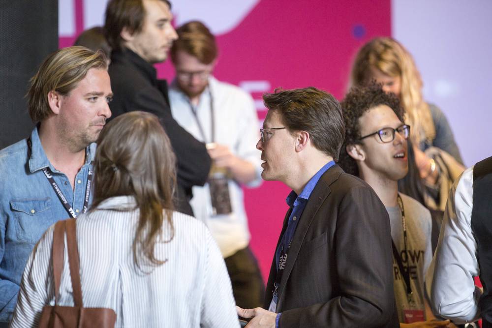 A group of people chat together near a backdrop reading 'TNW' at the conference.