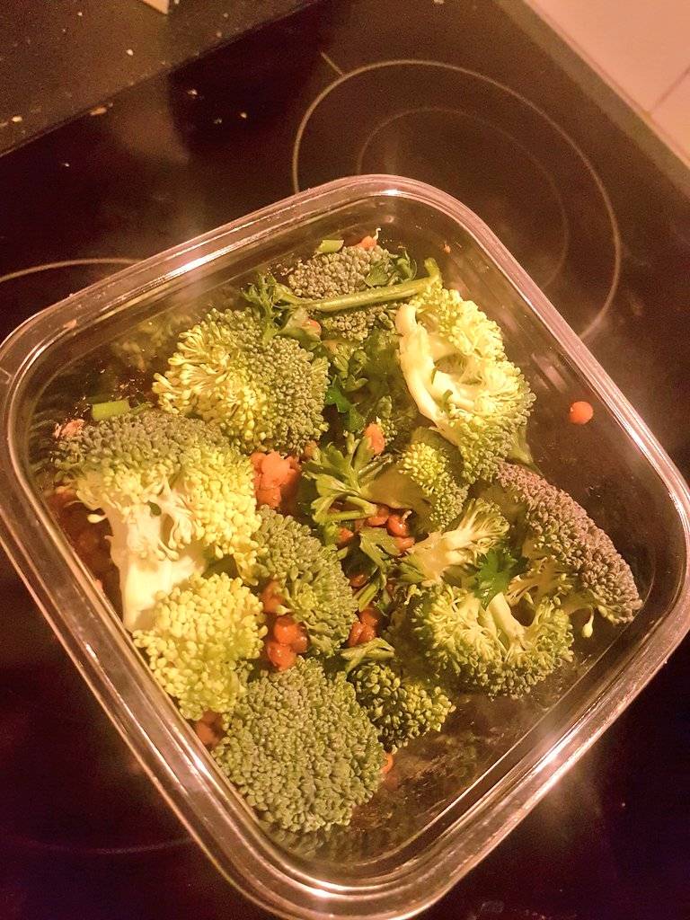 A plastic container holds steamed broccoli, cauliflower and carrots.