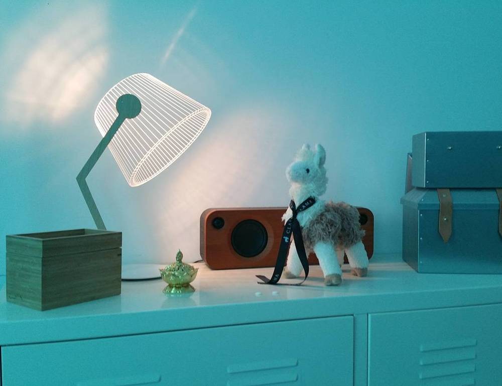 A collage of modern furniture and decor items, including a lamp and a stuffed toy animal, on a teal cabinet.