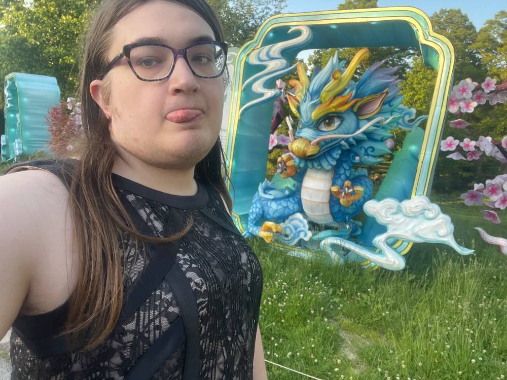 A trans woman wearing glasses and a black dress in front of an inflatable chinese dragon
