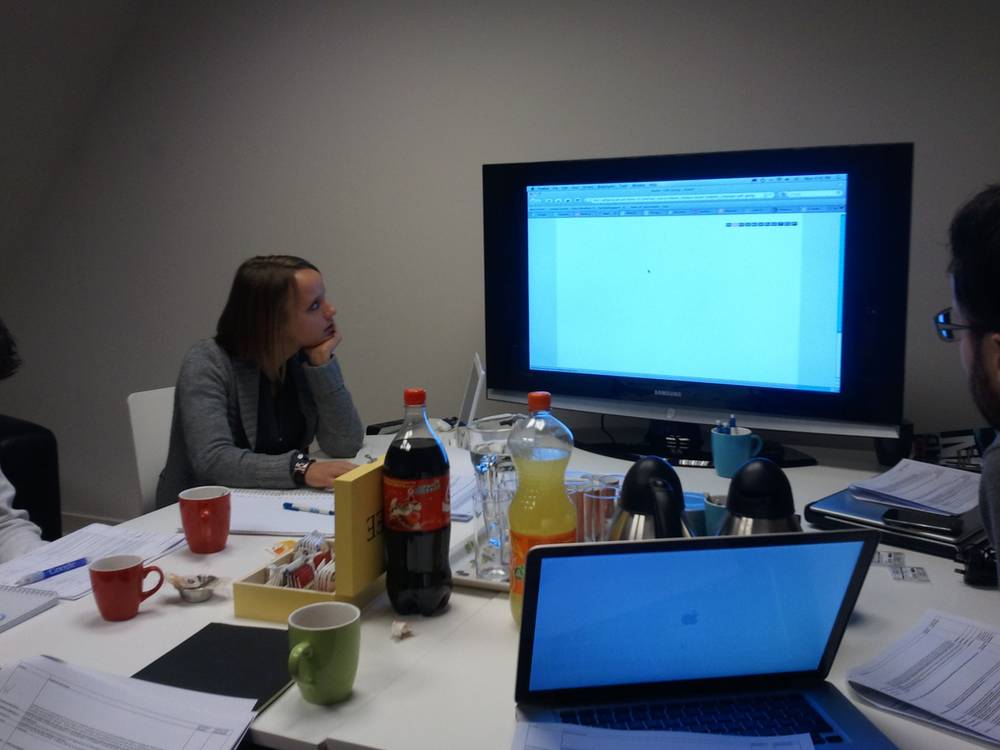 Colleagues sit around a table with laptops and drinks during a jury deliberation meeting.
