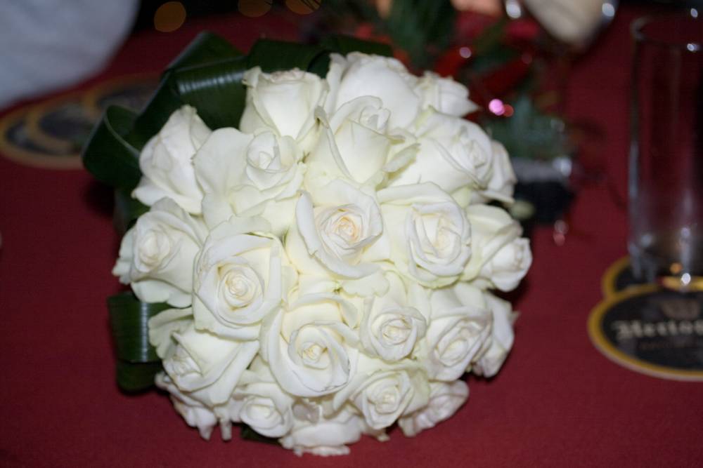 A round bouquet of white roses sits on a table at a wedding.