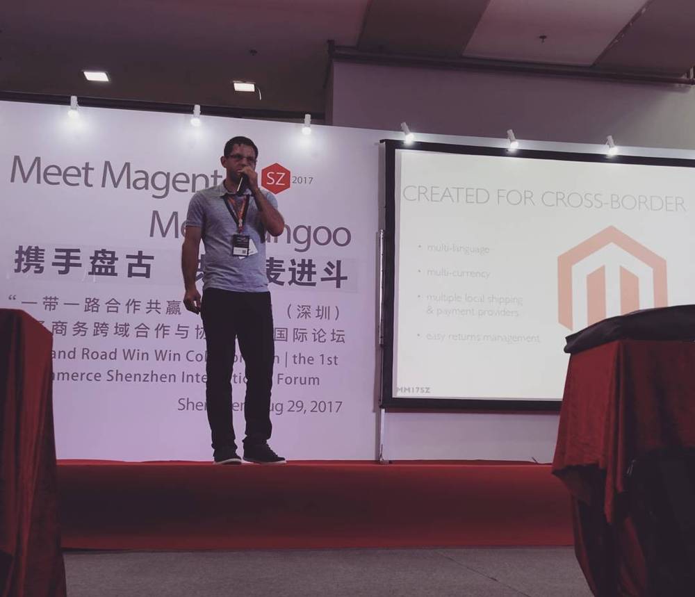 A man presenting on stage next to a slide titled "Created for Cross-Border," at the Meet Magento conference.