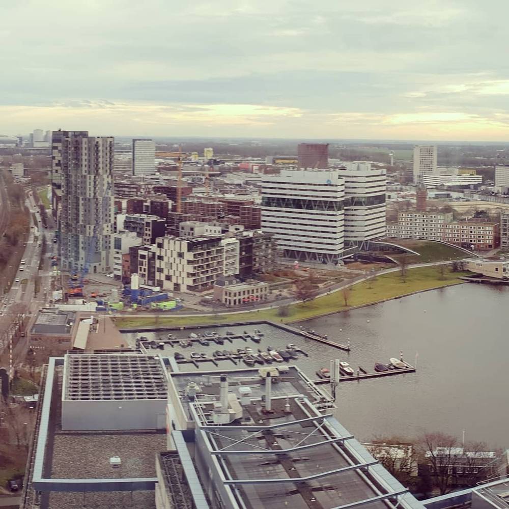 Aerial view of Rotterdam's skyline with modern buildings, a marina and cranes under an overcast sky.