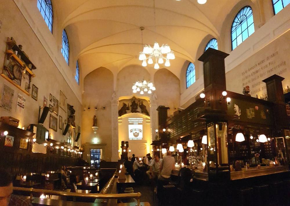 Interior of a grand bar inside a former church, with high vaulted ceilings and chandeliers, in Utrecht.