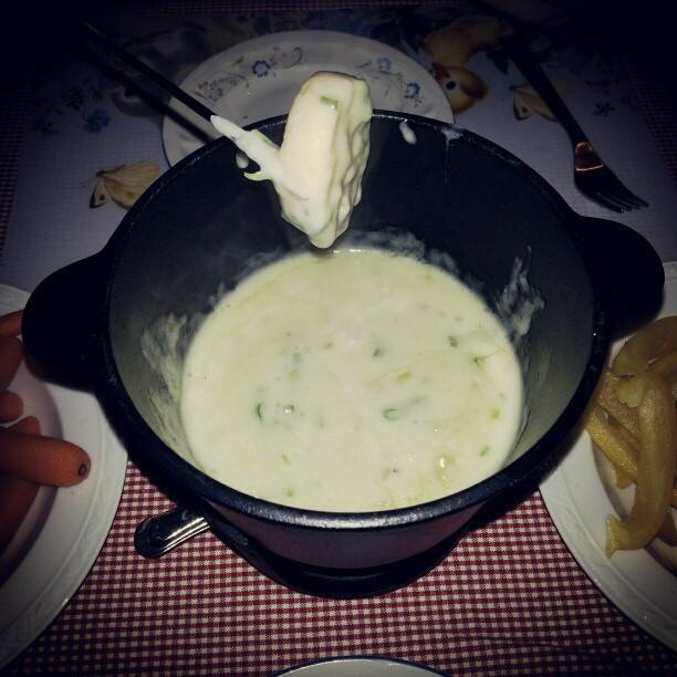 A piece of bread being dipped into a bowl of cheese fondue.