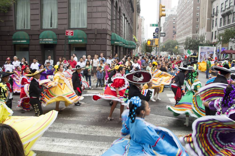 Dancers in wide traditional skirts twirl through a crowded parade route.