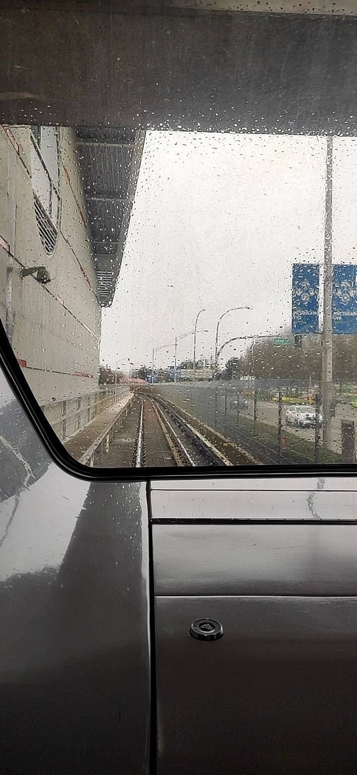 Photo from inside the first row inside the train, it's a bright and rainy day, the sky is gray