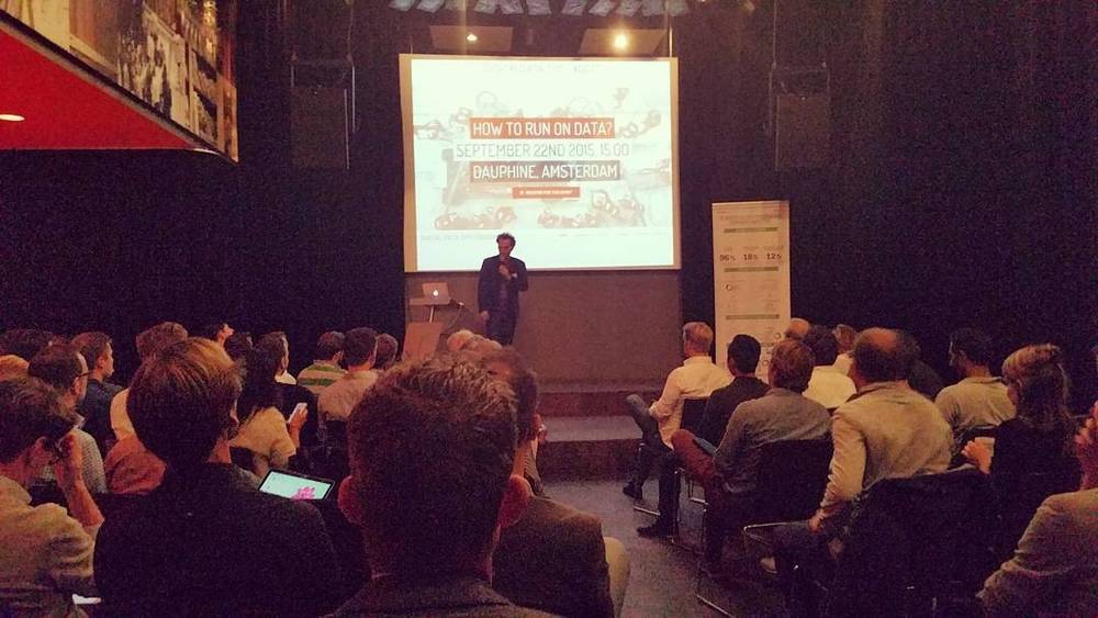 A speaker presenting on stage to a seated audience at a conference, with a slide reading "How to run on data?".