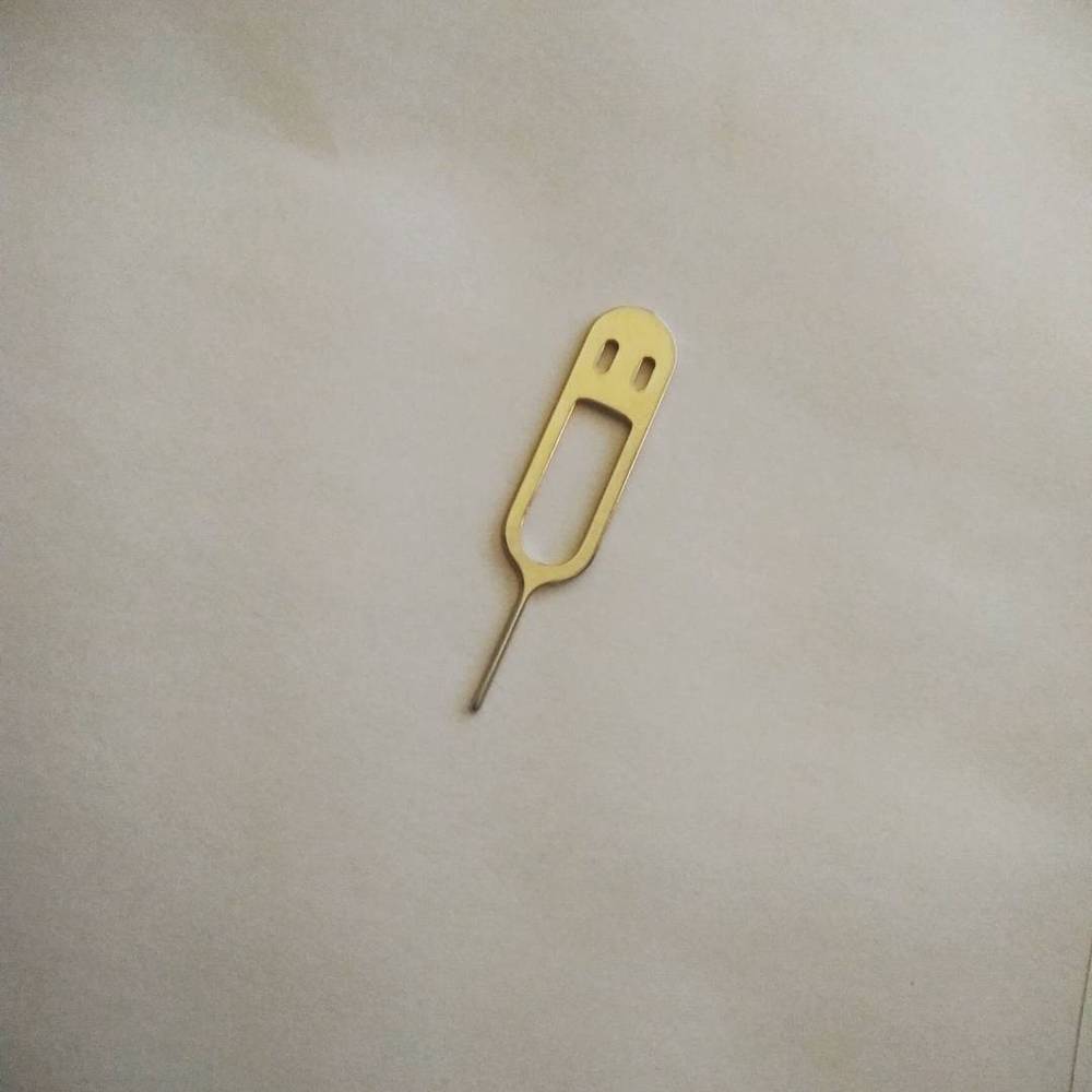 A gold SIM card ejector tool lying on a plain surface.