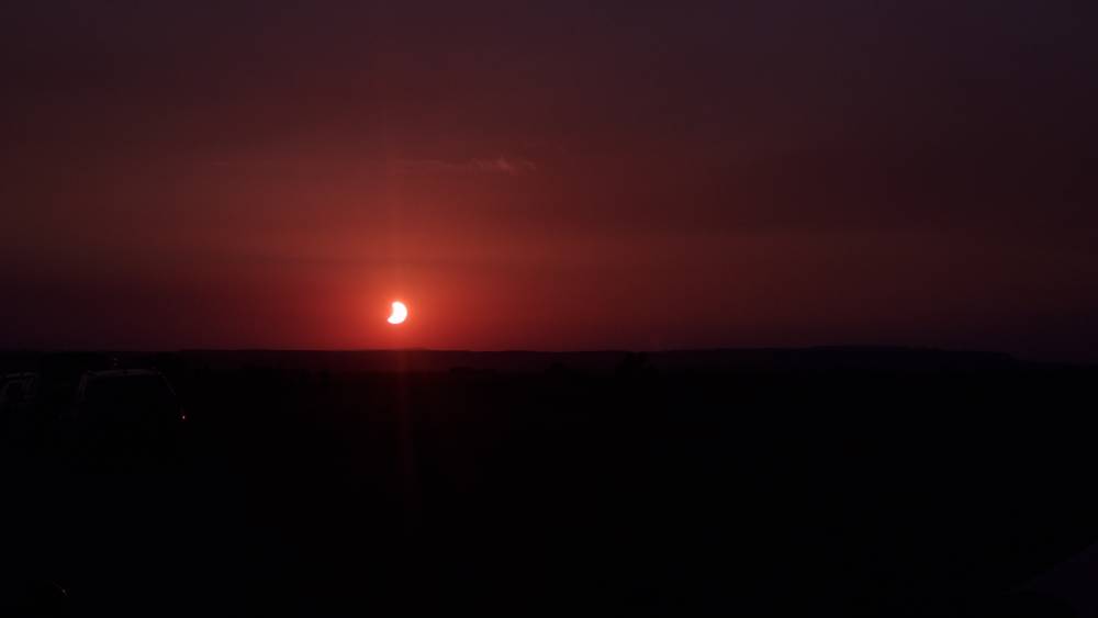 A partial solar eclipse shows a crescent sun in a reddish sky.