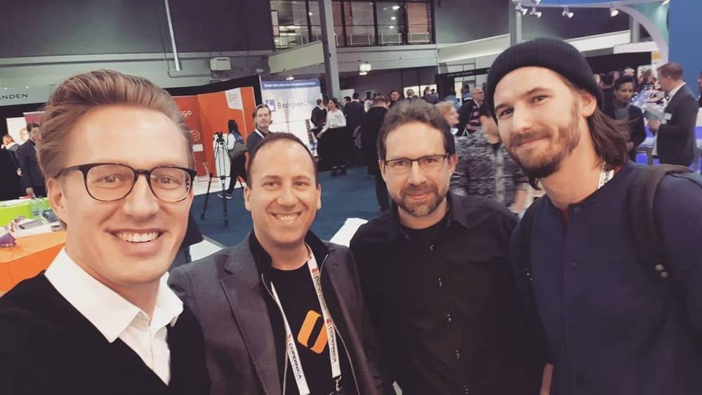 Four men pose together smiling at a conference expo hall.