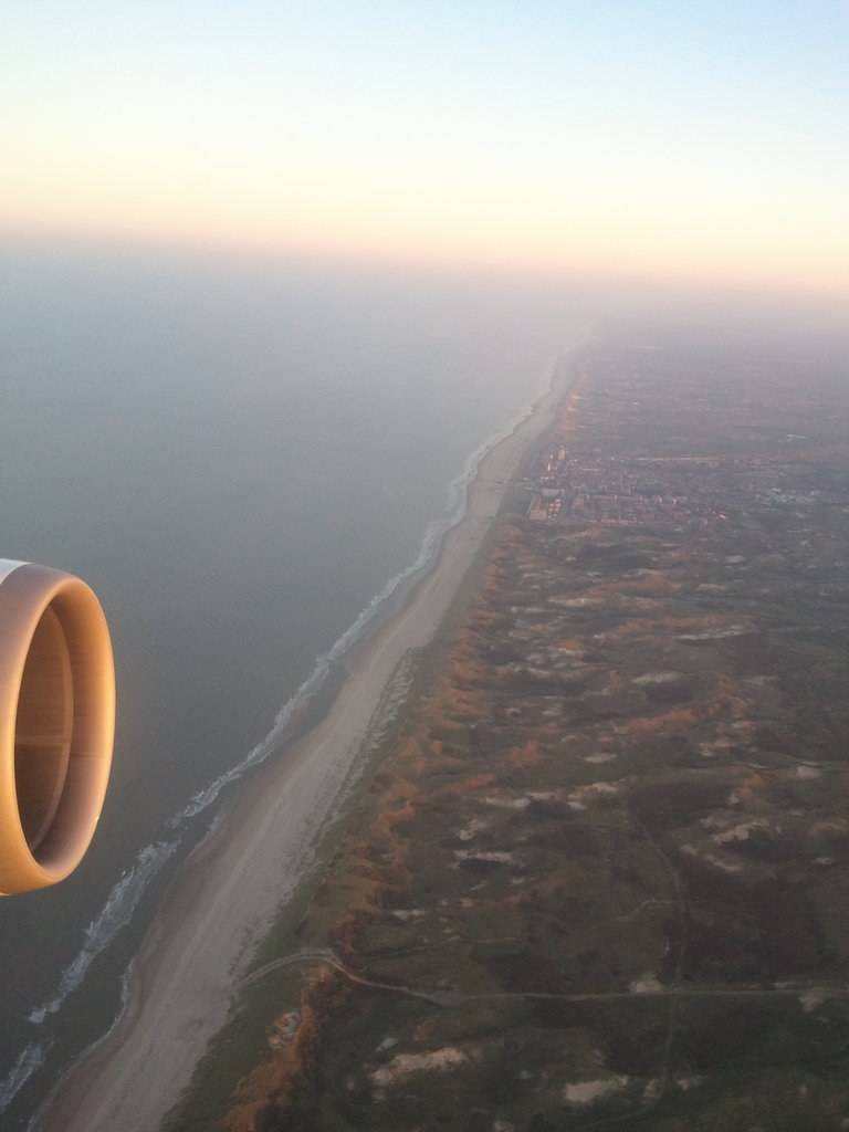 An aerial view from the plane shows a coastline and dunes as the flight returns to the Netherlands.