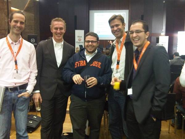 Five conference attendees with lanyards posing and laughing together at an evening event.