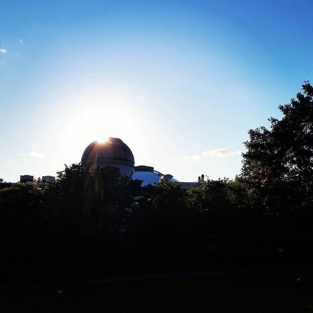 Silhouette of a domed observatory building against a bright sky with the sun behind it.